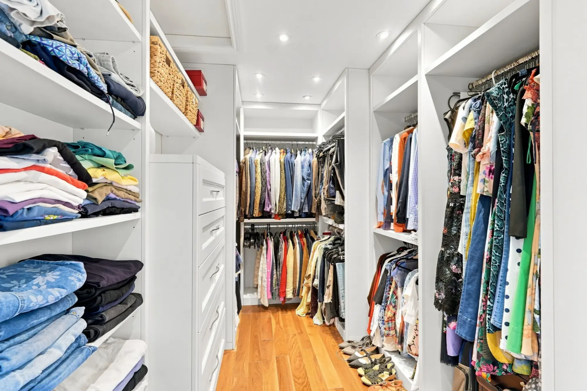 Walk-in wardrobe with white fitted shelving, hanging clothes, folded garments and wood flooring