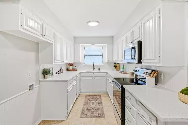 Bright galley kitchen with white cabinets, quartz countertops, stainless steel appliances, and a large window bringing in natural light in a Fort Worth home.