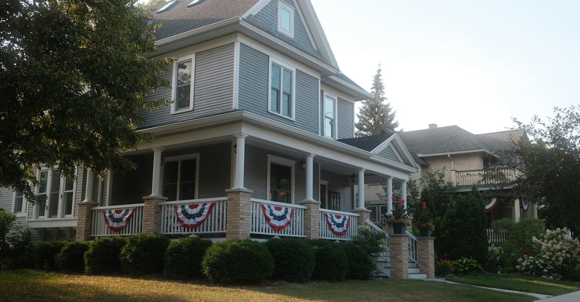 A gray two-story house with a covered front porch on a residential street
