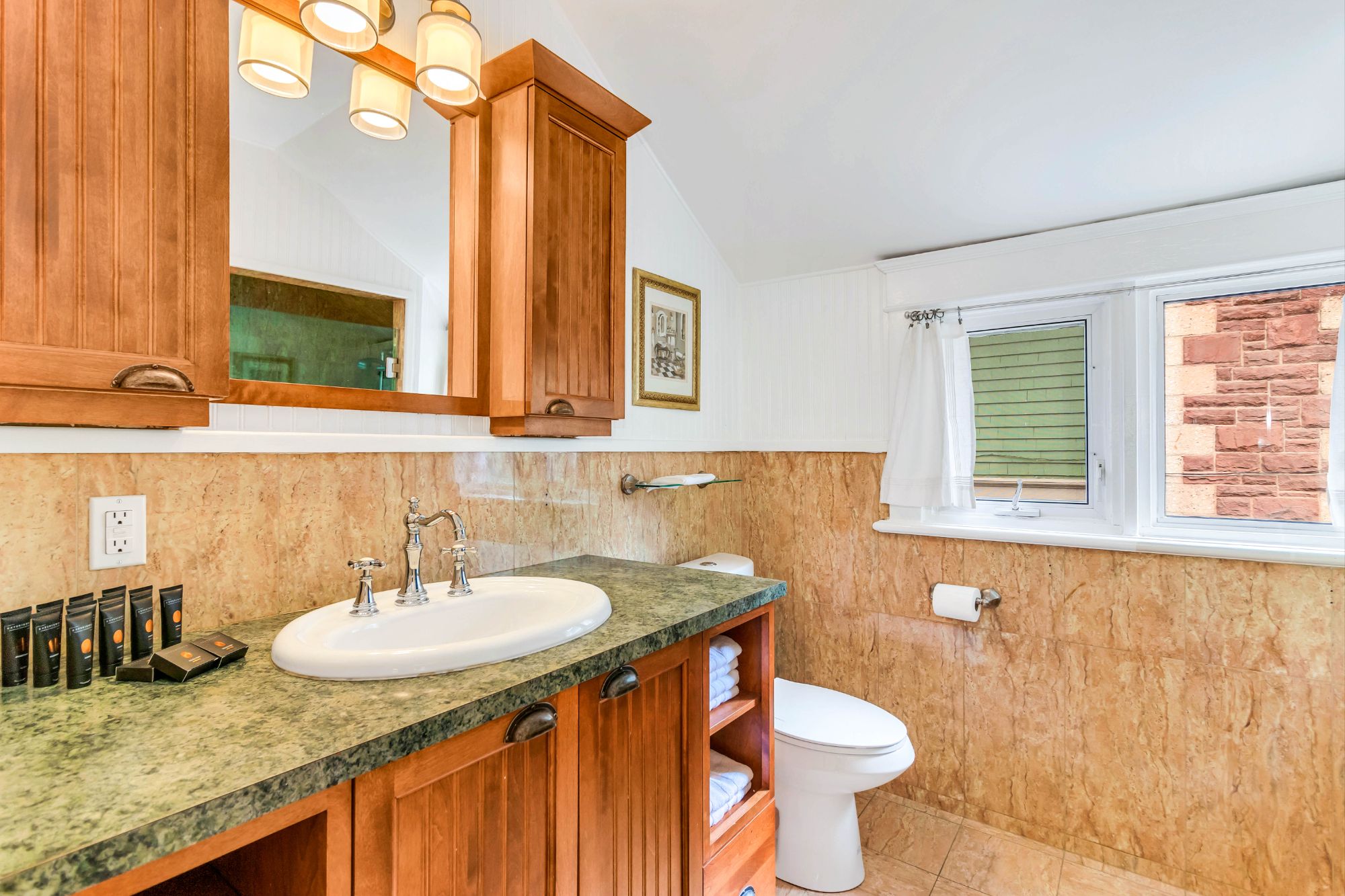 Second-floor bathroom at 134 Church Street Moncton with vintage stone tile walls, warm wood cabinetry and green marble countertop
