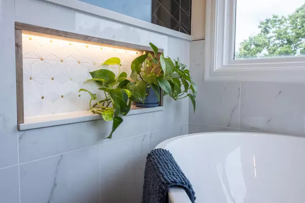 Modern bathroom with marble tile, illuminated niche, greenery, and freestanding soaking tub