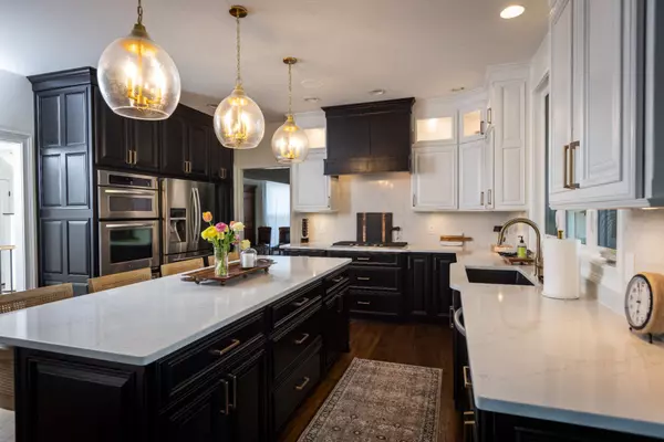 Modern renovated kitchen with dark cabinetry, white quartz countertops, double ovens, and pendant lighting — luxury home interior.