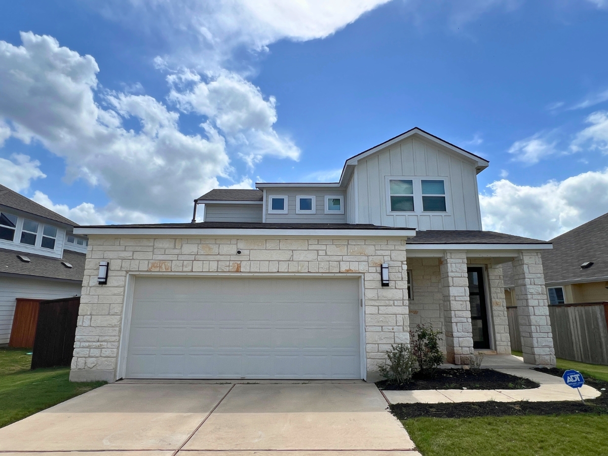 Two-story Orchard Ridge Liberty Hill Texas home with white exterior finishes, limestone façade, and covered front entry