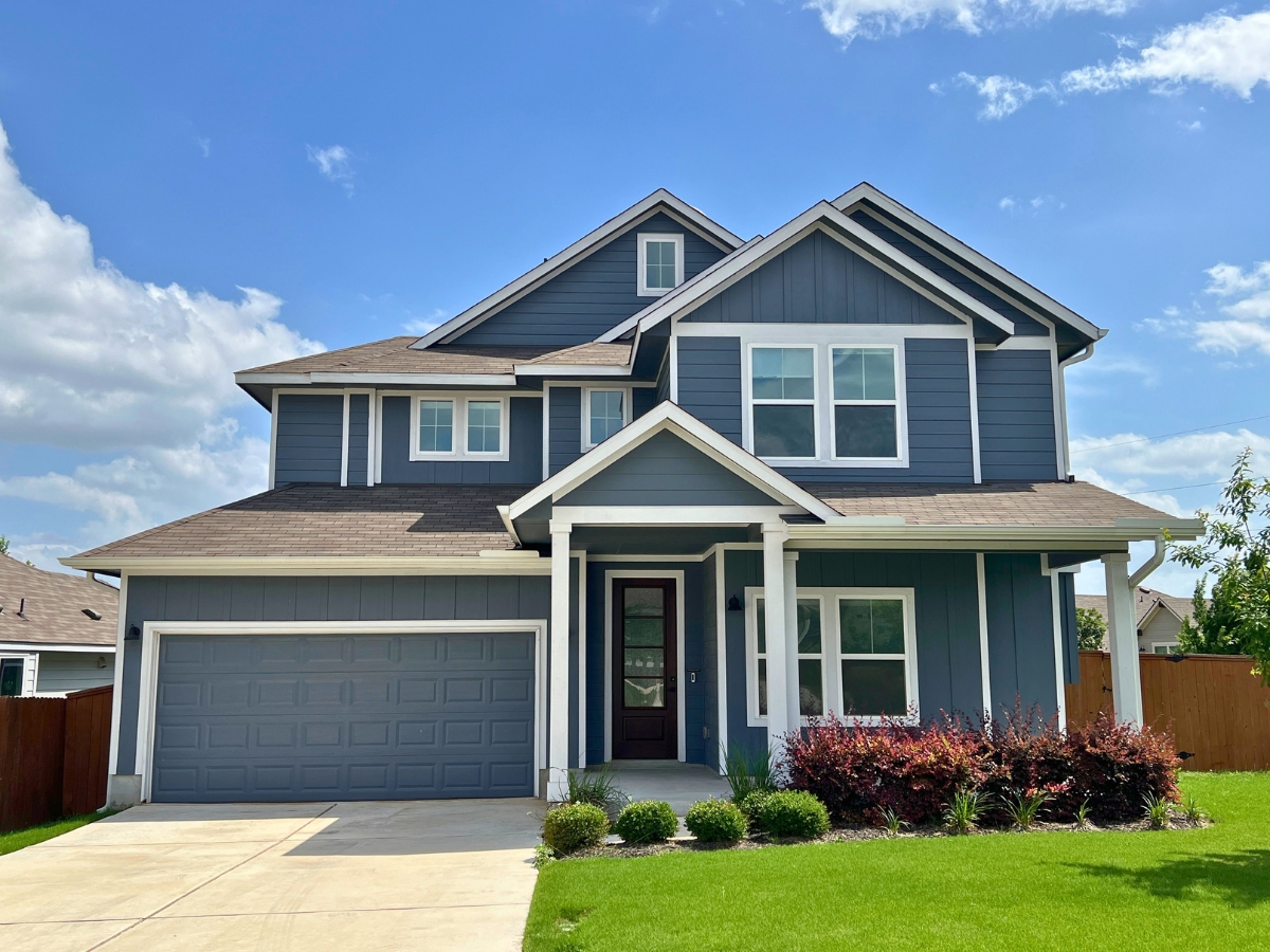 Two-story blue Orchard Ridge Liberty Hill Texas home with white trim details, prominent front windows, and covered porch entry