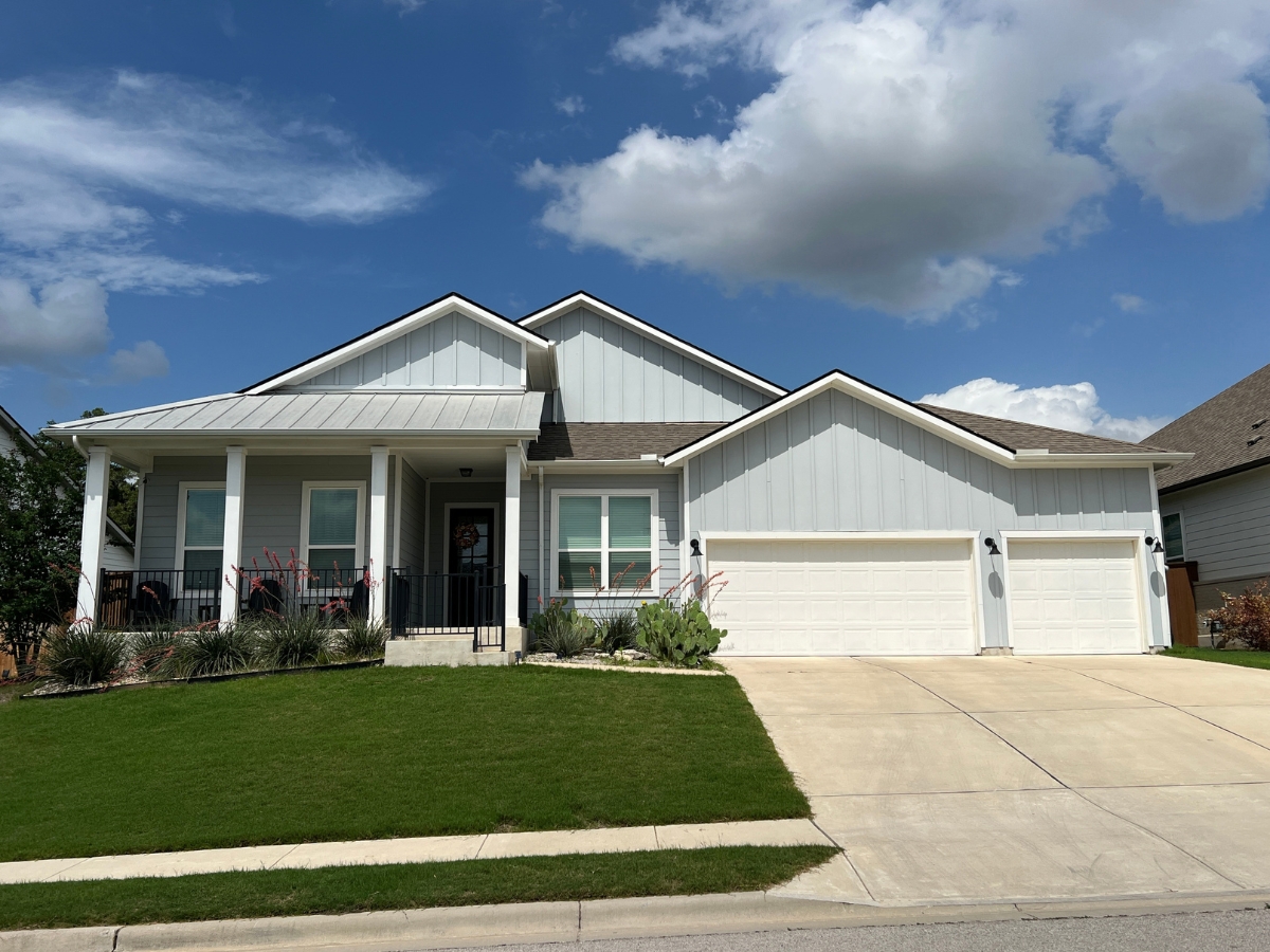 Single-story Orchard Ridge Liberty Hill Texas home with light gray exterior, wide front porch, and three-car garage layout