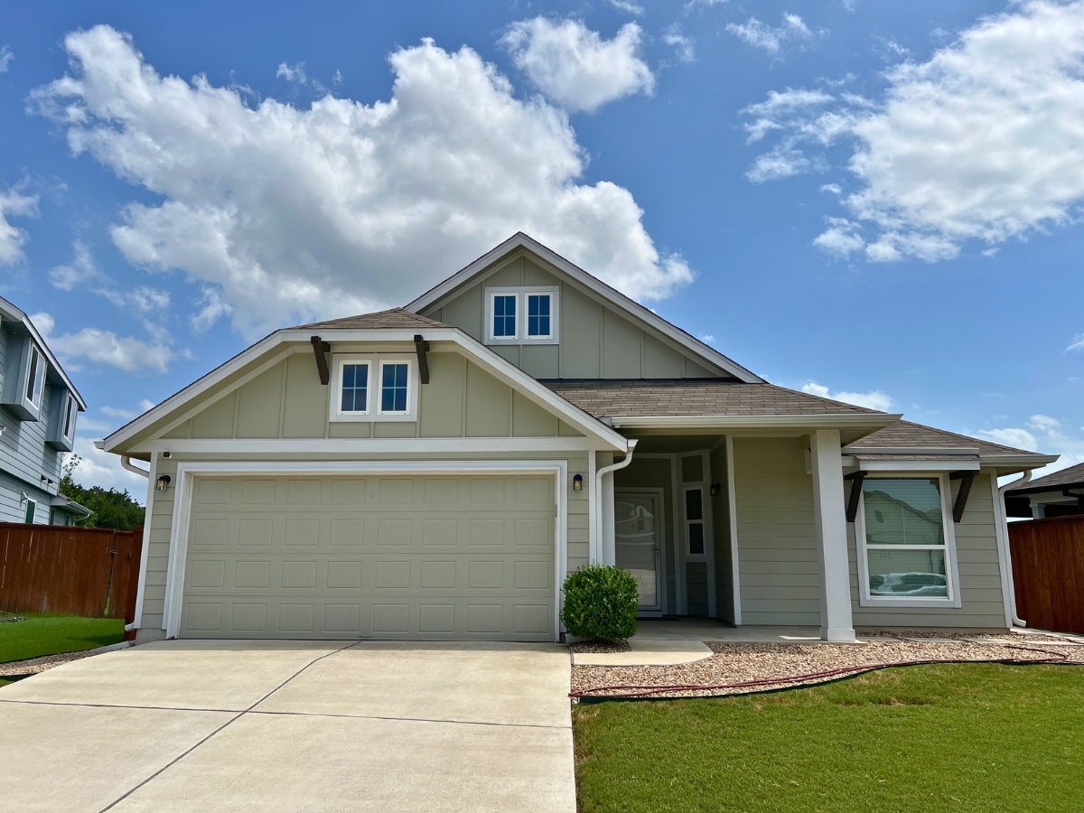 Single-story Orchard Ridge Liberty Hill Texas home with soft green siding, decorative trim details, and covered front entry