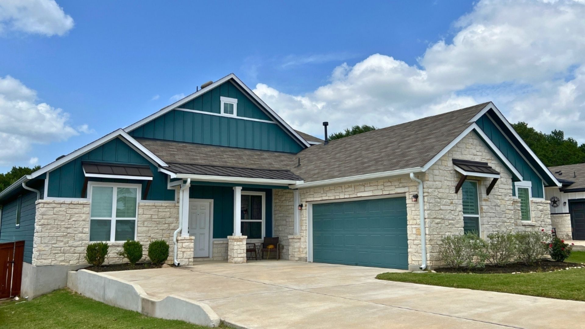 Single-story Orchard Ridge Liberty Hill Texas home with blue board-and-batten siding, limestone accents, and covered front porch