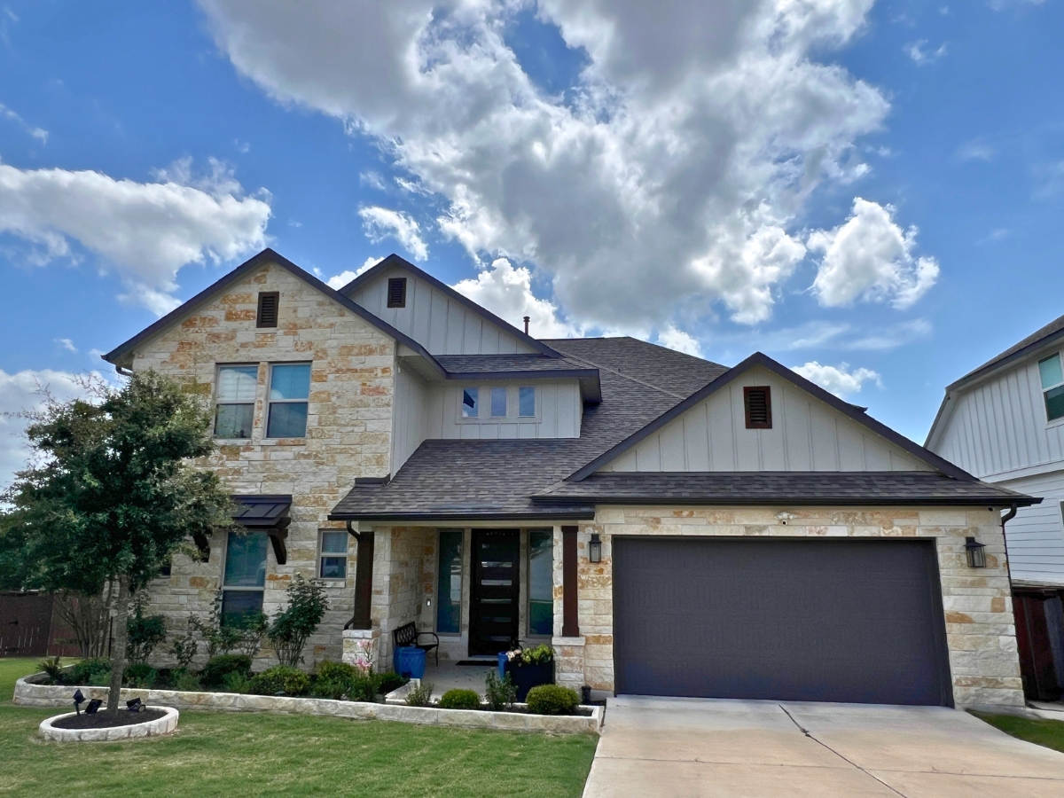 Two-story Orchard Ridge Liberty Hill Texas home with limestone exterior, dark garage door, and covered entryway