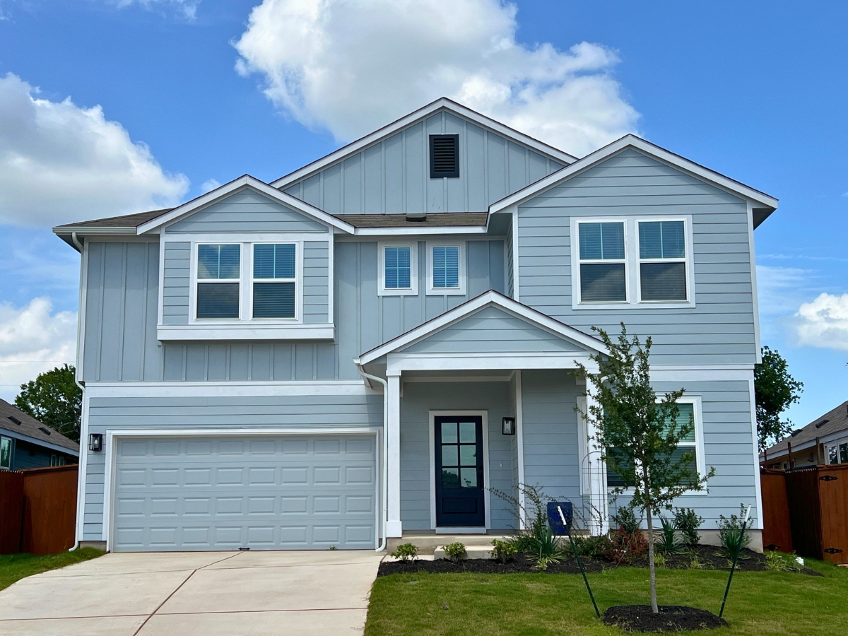 Two-story home in Orchard Ridge Liberty Hill Texas with light blue exterior siding, covered front porch, dark entry door, and attached two-car garage