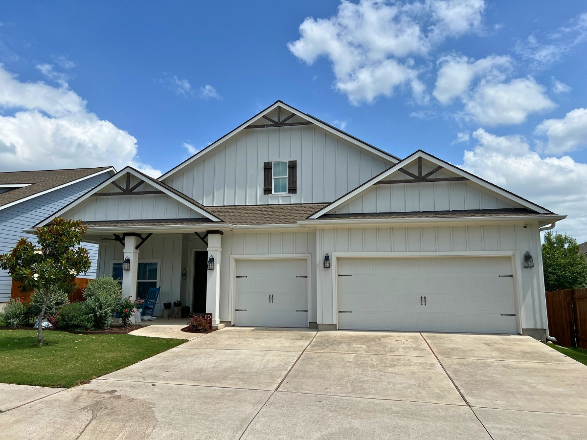 Large white board-and-batten home in Orchard Ridge Liberty Hill Texas with covered front porch and three-car garage