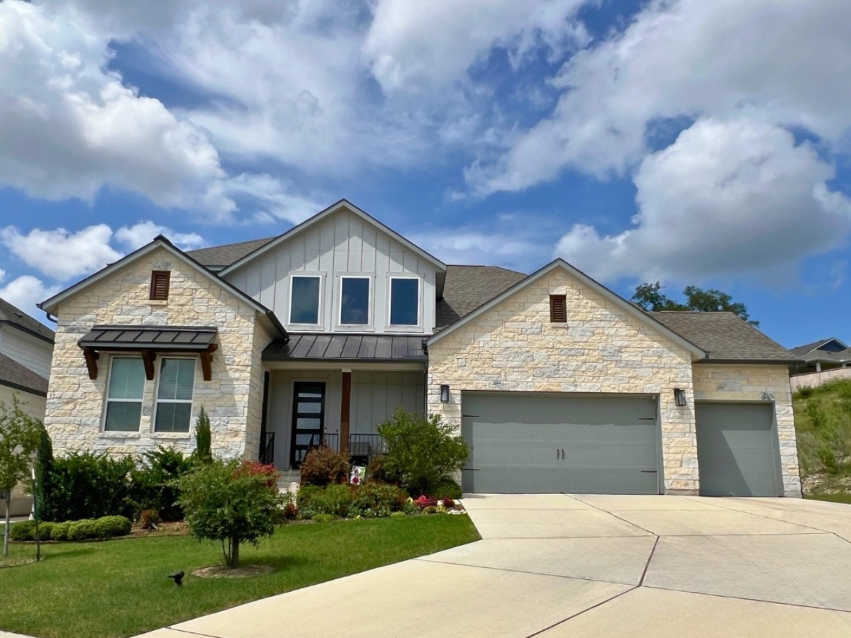 Large stone and modern farmhouse-style home in Orchard Ridge Liberty Hill Texas with three-car garage, mixed exterior materials, and upgraded front landscaping