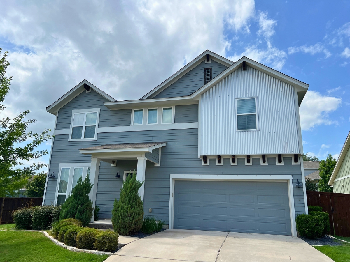 Large two-story home in Orchard Ridge Liberty Hill Texas with blue-gray siding, corrugated accent panel, and covered front porch