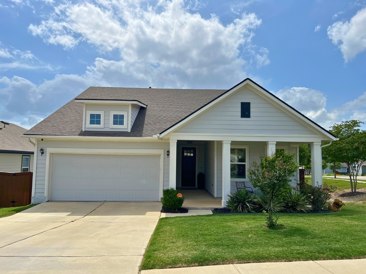 Single-story Orchard Ridge Liberty Hill Texas home with soft green exterior, front porch seating area, and cottage-inspired design