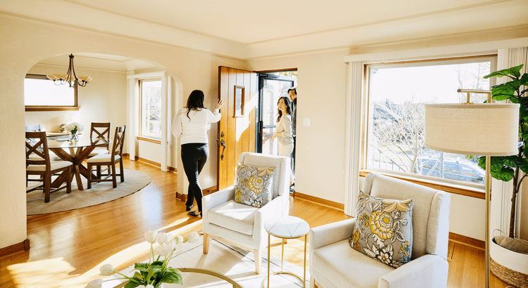 Realtor welcoming homebuyers into a bright living room during a home showing in San Diego County, illustrating improving affordability in 2025.