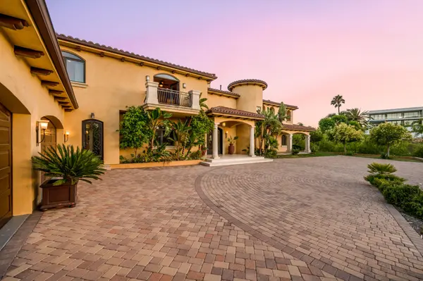 Luxury home exterior with paver circular driveway and balcony at sunset.