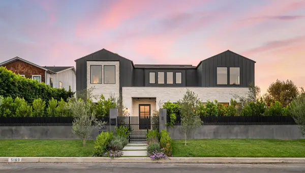 Contemporary luxury home with dark siding, stone facade, and gated entry at sunset.
