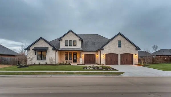 professional photo of Modern farmhouse-style home exterior in North Texas, light cream or warm white stone and stucco facade, black-framed windows, wood-toned garage doors, three-car garage, manicured but natural landscaping with native Tex