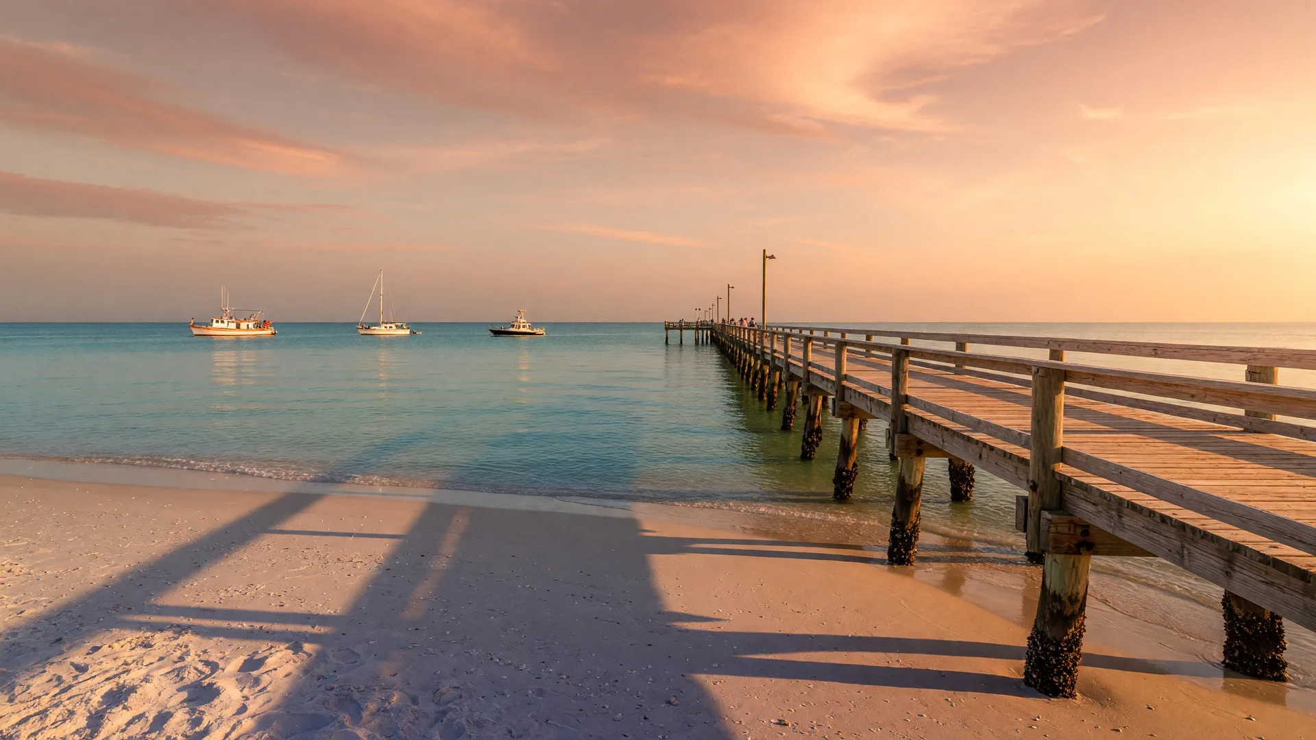 Golden hour view of the Alabama Gulf Coast with a pier extending into calm turquoise water and white sand beaches