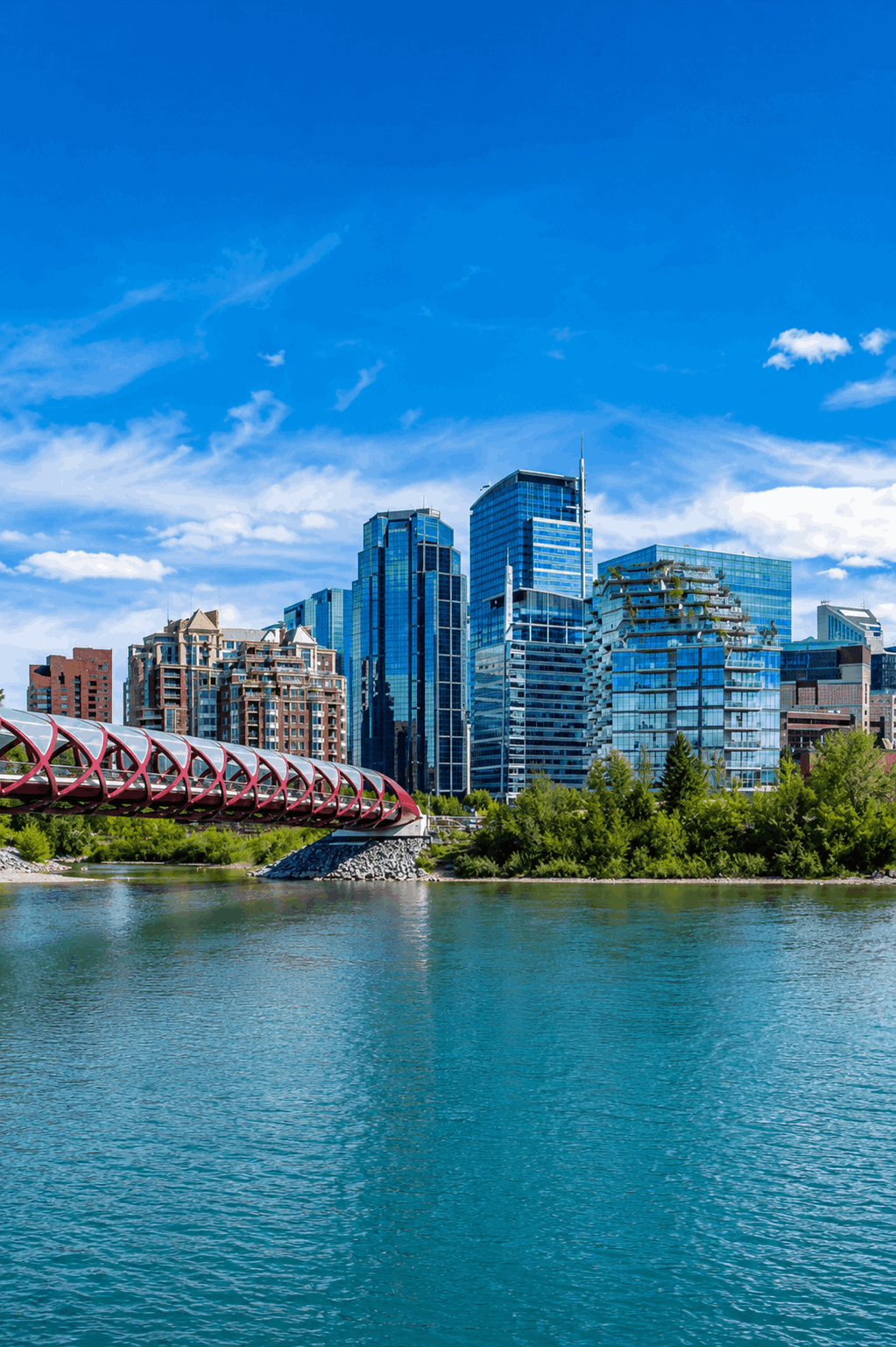 The Peace Bridge spans the Bow River with Calgary's downtown skyline rising behind it, showcasing riverfront pathways, modern development, and urban green space.