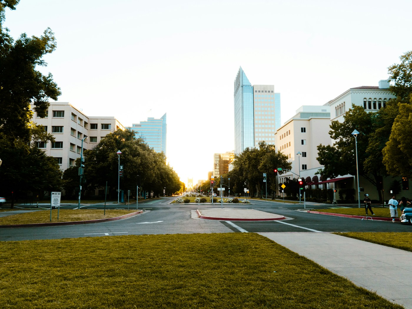 A wide city street lined with buildings and trees at sunset