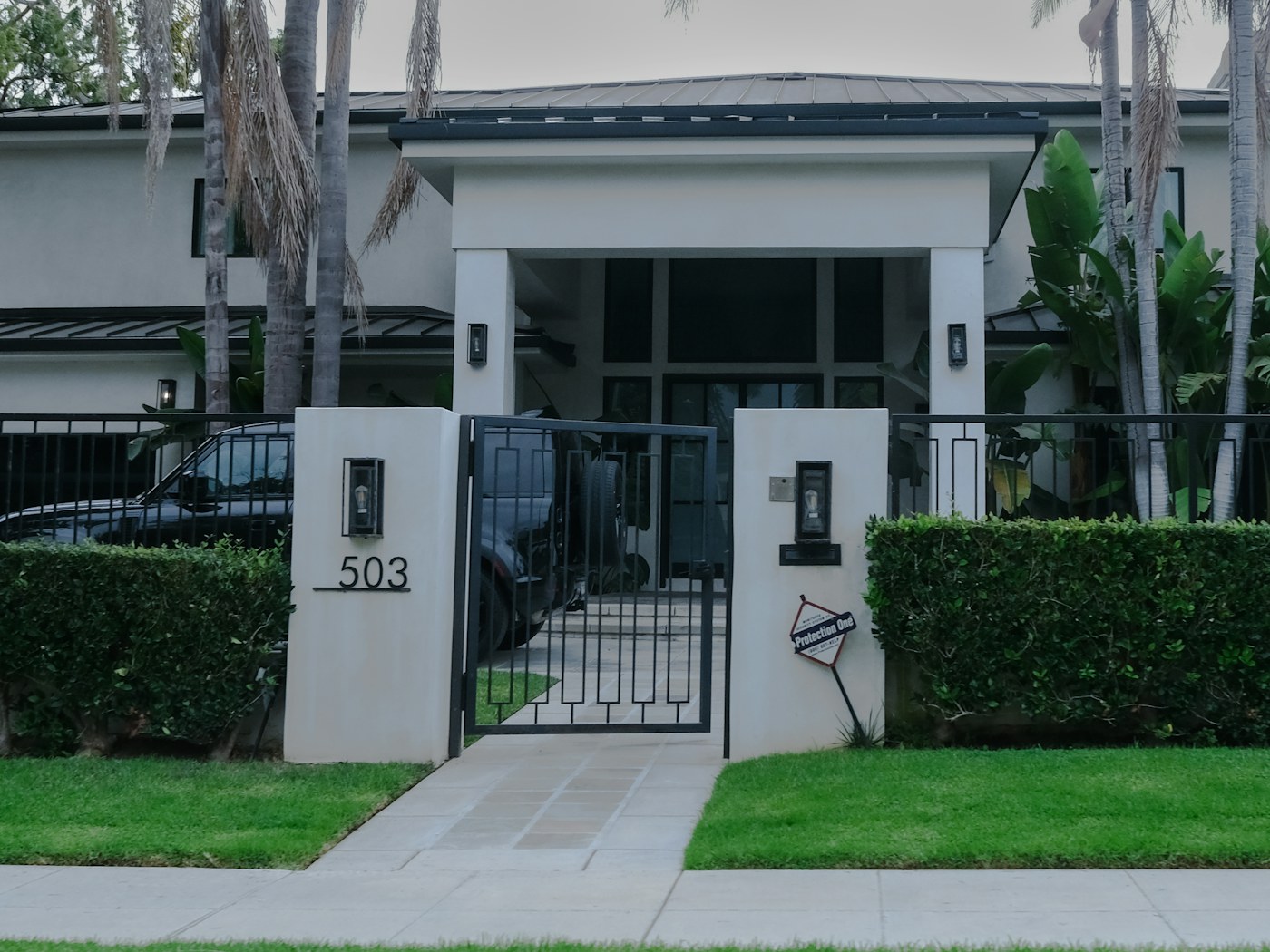 A modern home exterior with manicured hedges and a gated entry