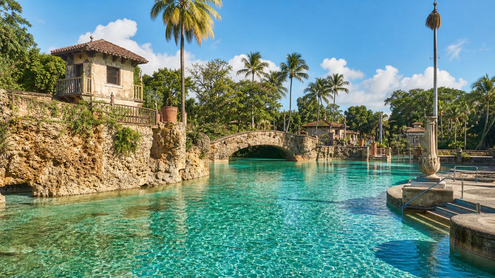 Historic Coral Gables pool architecture inspired by Venetian Pool, with coral rock, turquoise water, palms, and Mediterranean Revival details.