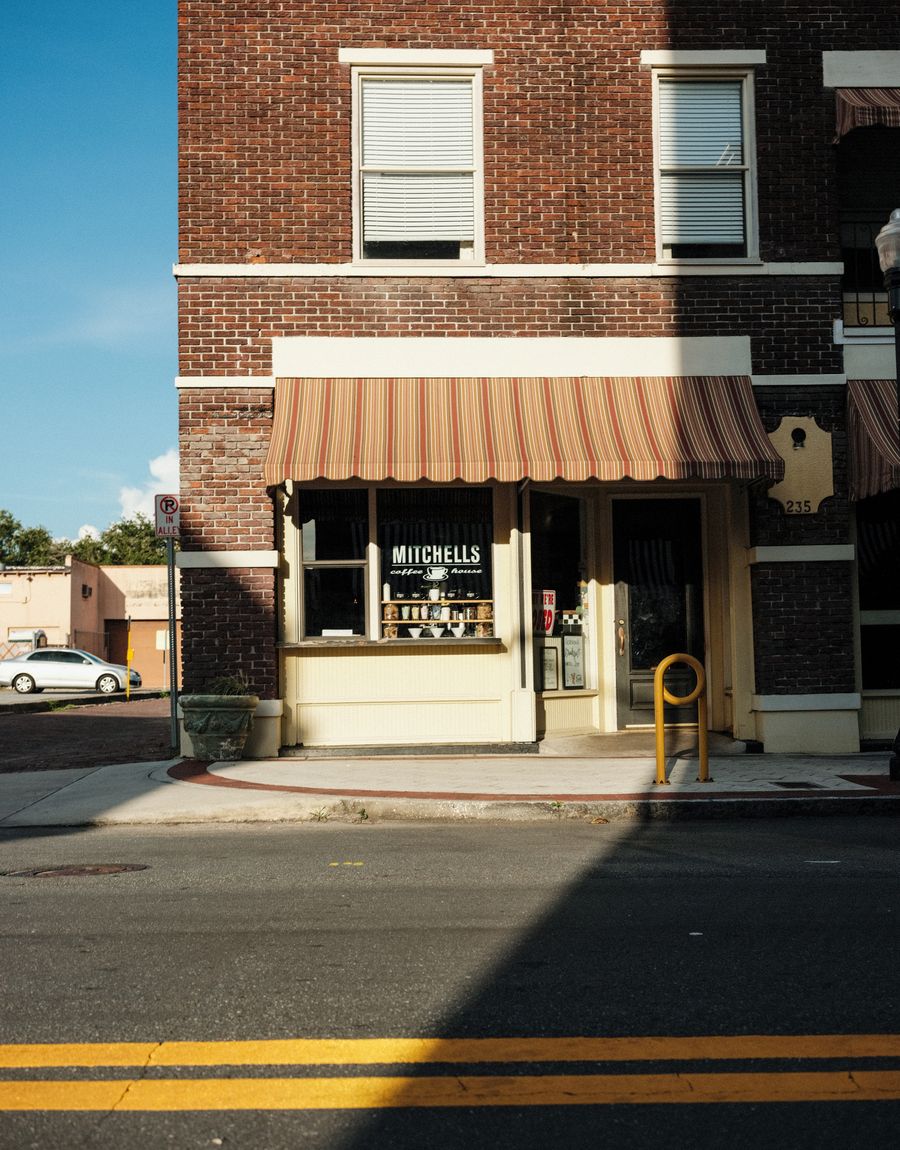 A brick storefront with a striped awning on a sunny small-town street corner