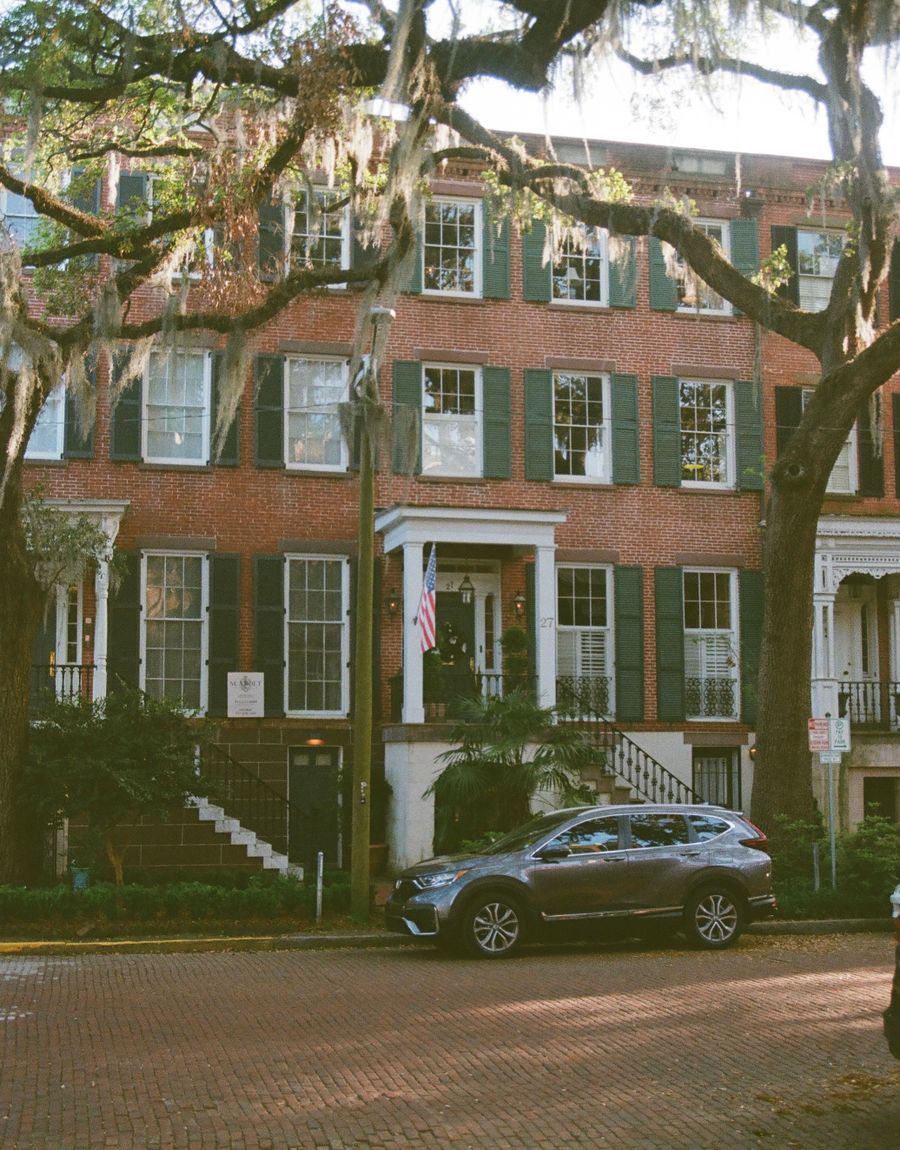 A brick townhouse with green shutters on a tree-lined historic street