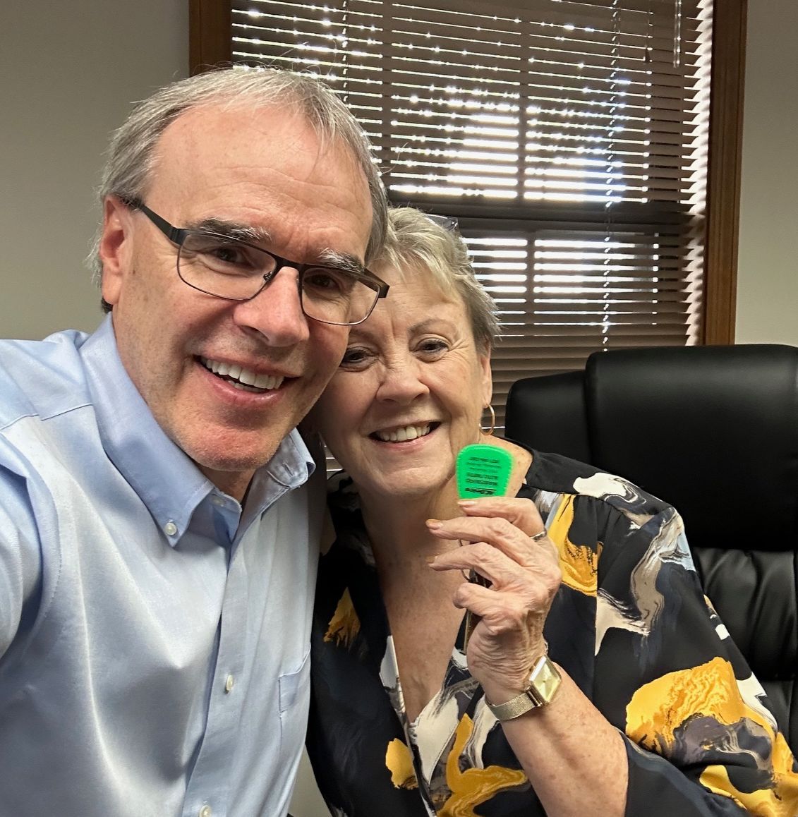 David Campbell realtor sits next to Phyllis as she holds a house key. They're both facing the camera, smiling.