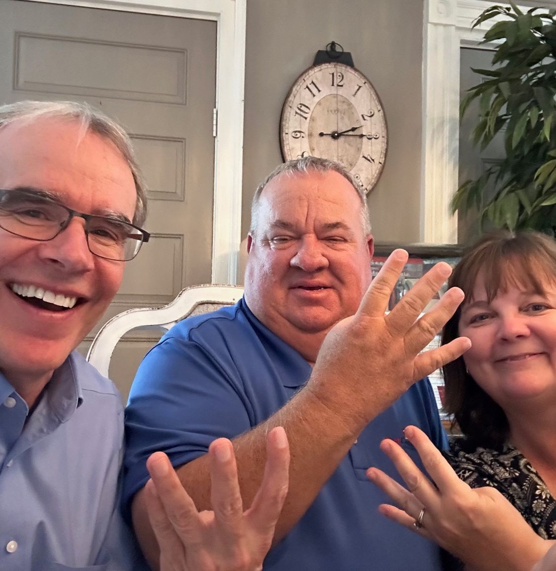 David Campbell realtor sits next to both Chris and Cindy as all three of them hold up four fingers while facing towards the camera, smiling.