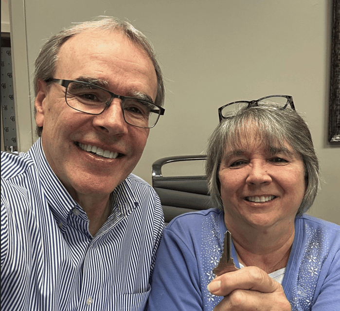 David Campbell realtor sits next to Terri while both of them smile towards the camera. Terri is holding a house key.