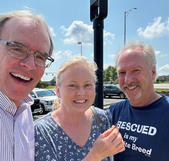 David Campbell realtor standing next to both Rob and Dana as they all face the camera, smiling. Dana is holding a house key.