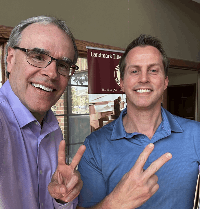 David Campbell realtor stands next to Erich as they both hold up two fingers, smiling towards the camera.