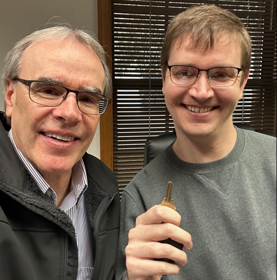 David Campbell realtor stands next to James as they both face towards the camera, smiling. James is holding up a house key.
