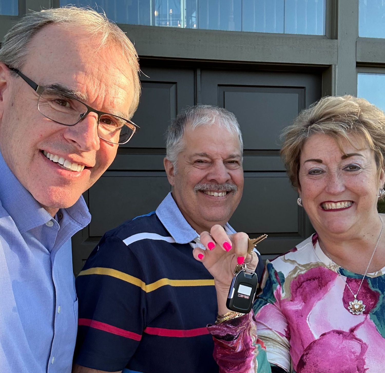 David Campbell, realtor, stands next to Maryann and another man as they all look towards the camera, smiling. Maryann is holding house keys.