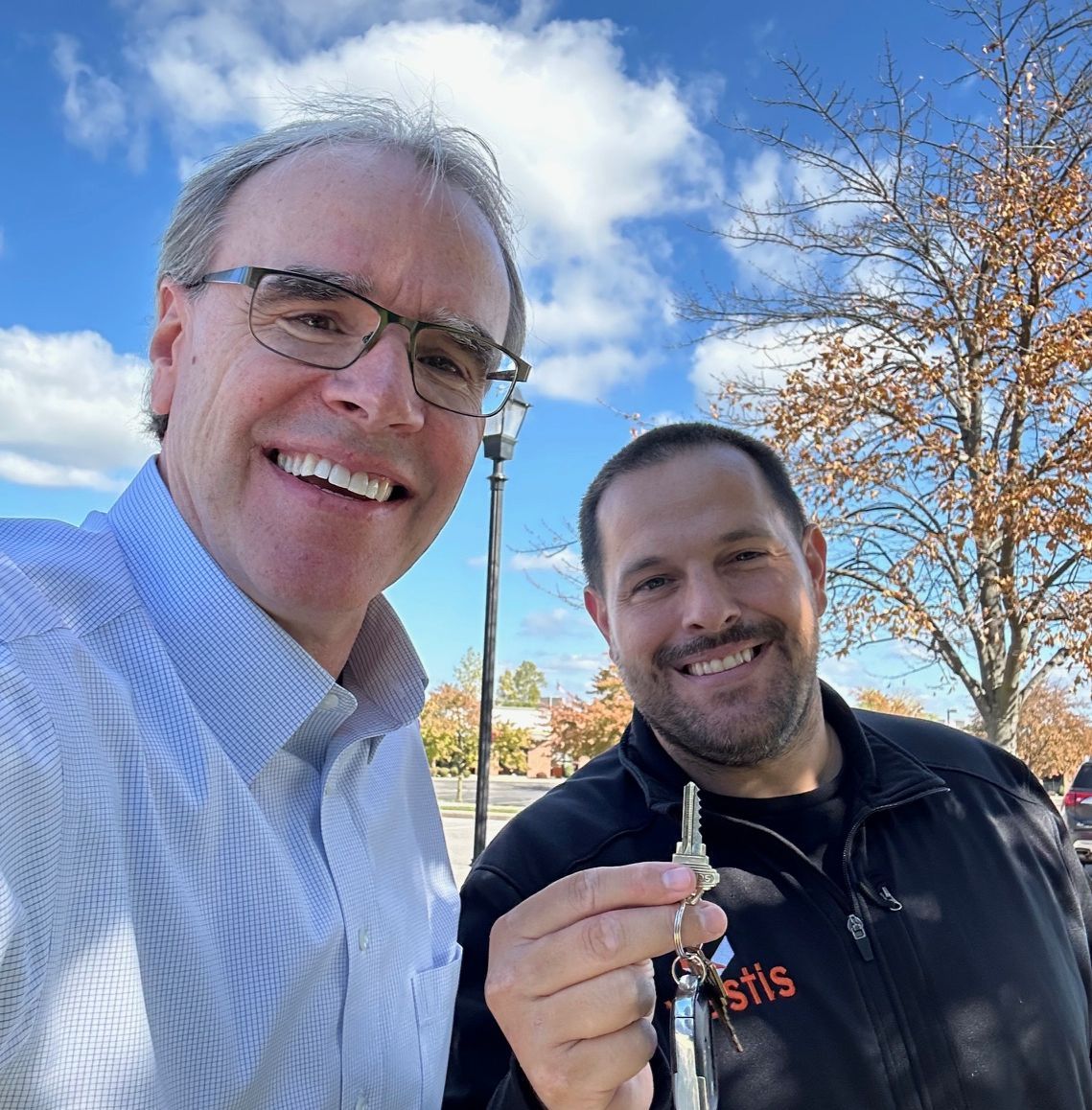David Campbell, realtor, stands next to Justin as they both face towards the camera, smiling. Justin is holding a house key.