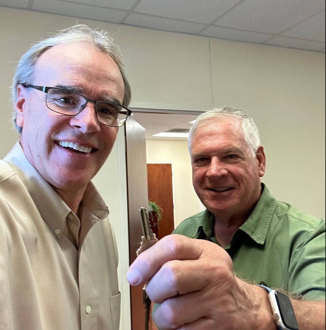 David Campbell, realtor, stands next to Colby as they both face towards the camera, smiling. Colby is holding up a house key.