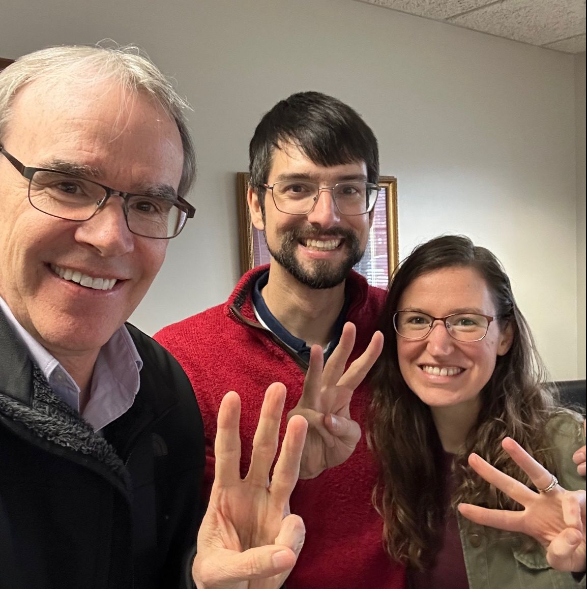 David Campbell, realtor, stands next to both Chase and Hannah as they all face towards the camera smiling. All three are holding up three fingers.