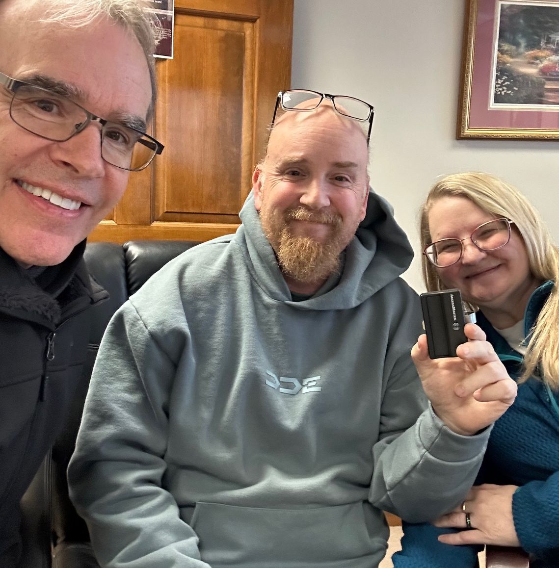 David Campbell realtor, sits next to both Steve and Rita as the all face towards the camera, smiling. Sam is holding up a garage door opener.