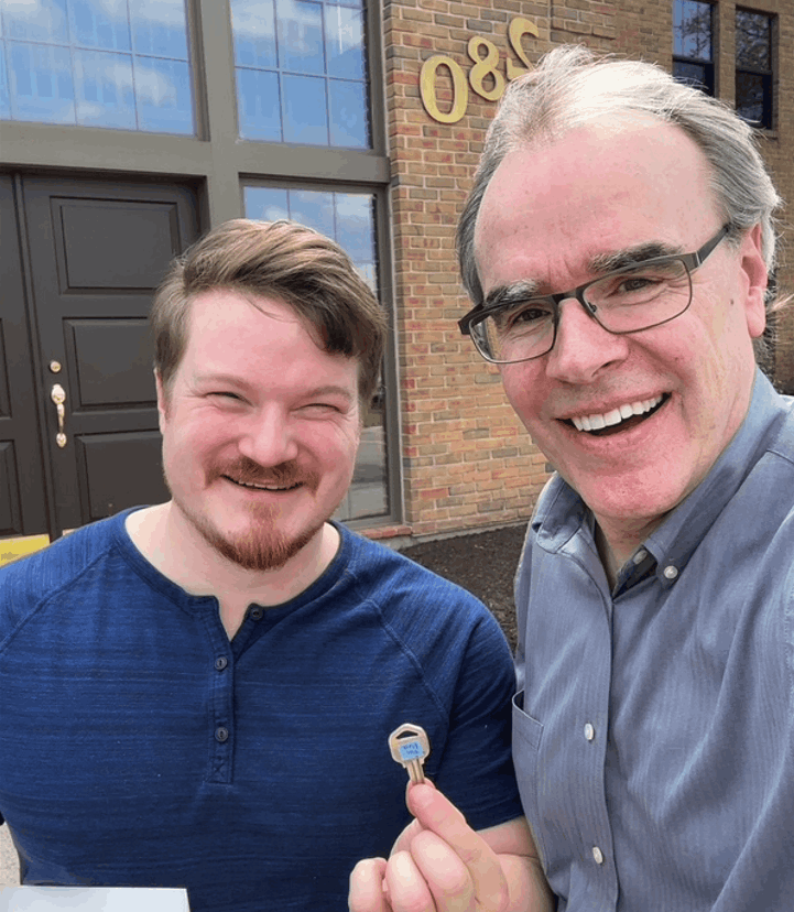 David Campbell is standing the right of a man who's holding a house key. They are both facing the camera, smiling.