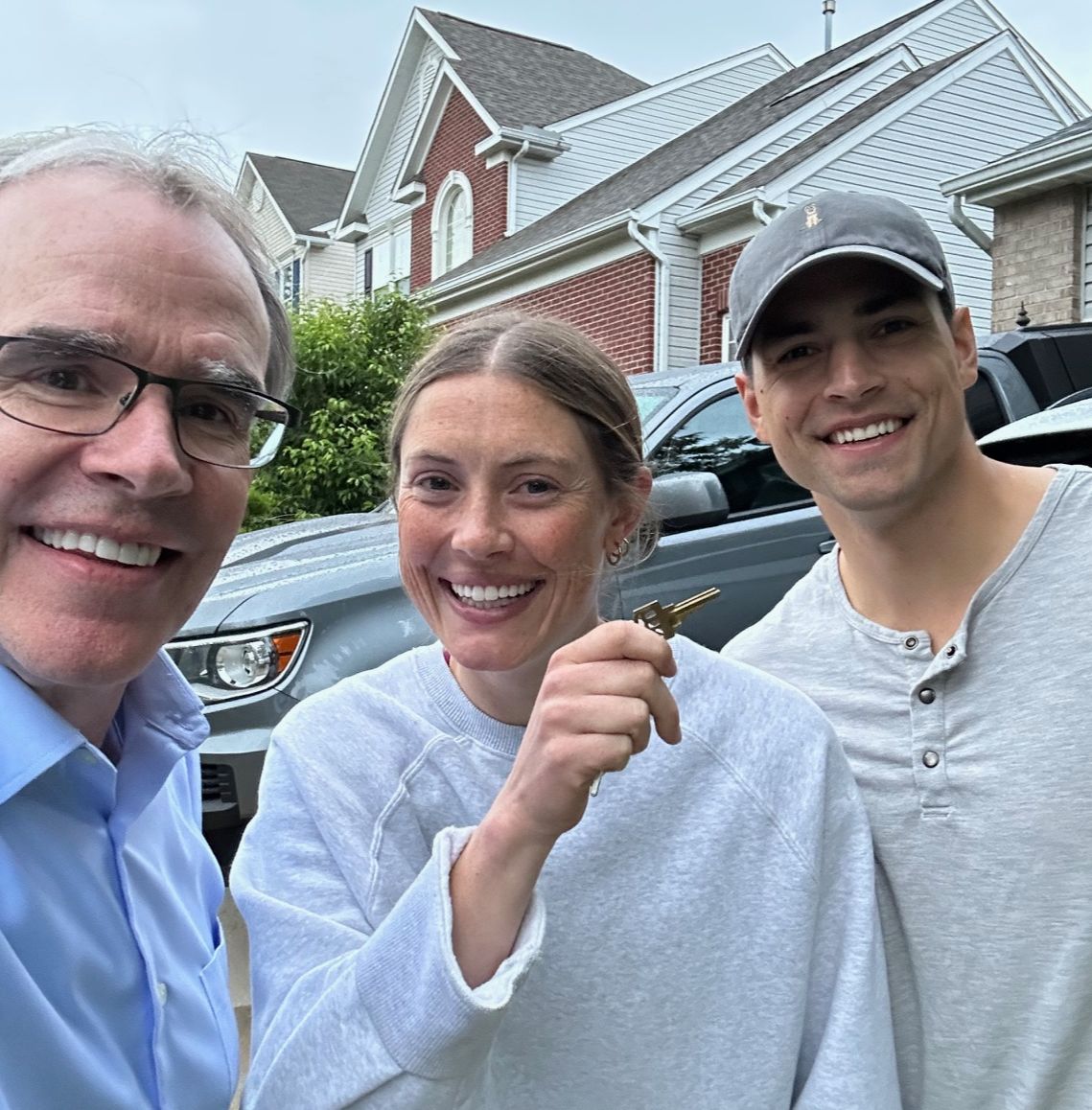 David Campbell, Realtor is standing beside a man and woman holding a house key. They're all facing towards the camera, smiling.