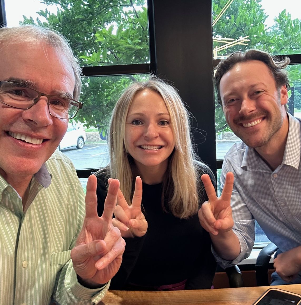 David Campbell, Realtor sits next to a man and woman. They're all facing towards the camera, smiling while holding up two fingers after a successful home purchase.