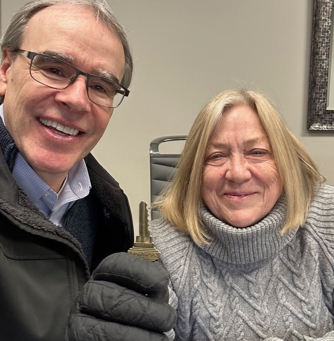 David Campbell, realtor stands next to Ann after a successful condo sale. They're both smiling while Ann holds up a house key.