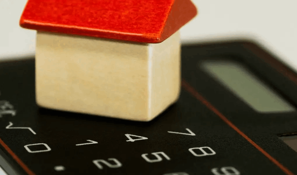Stock photo of a tiny wooden house on top of a calculator.