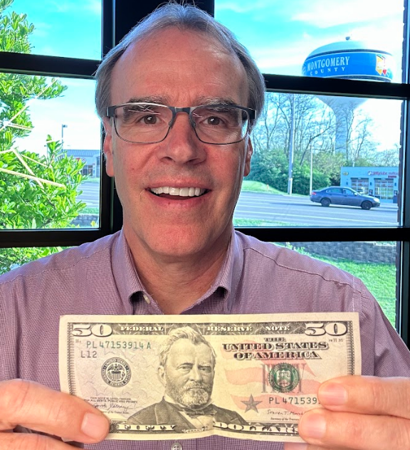 David Campbell realtor, holds up a $50 bill towards the camera, smiling.
