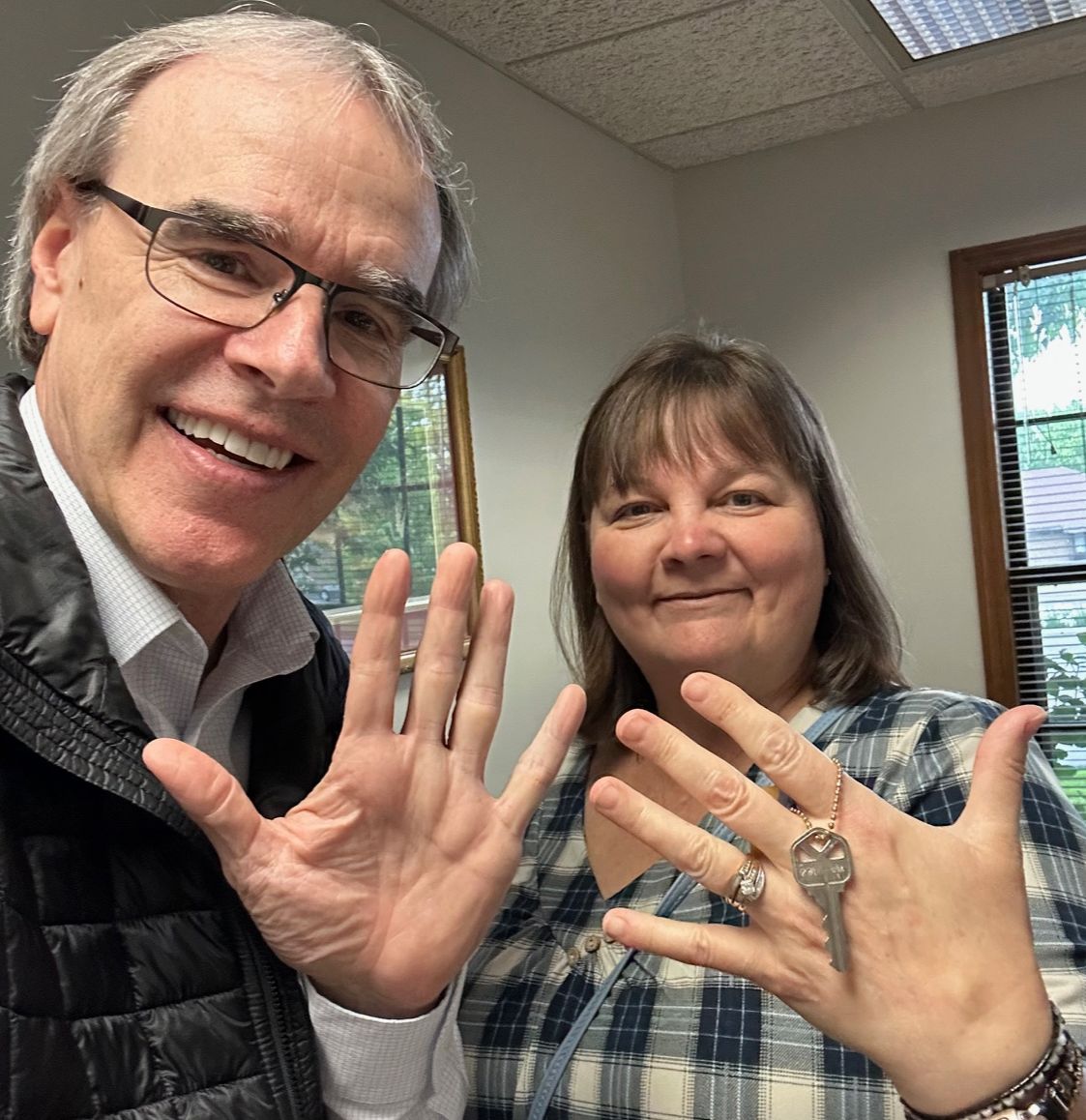 David Campbell, realtor stands next to Cindy as they hold up five fingers. Cindy is holding up a house key.