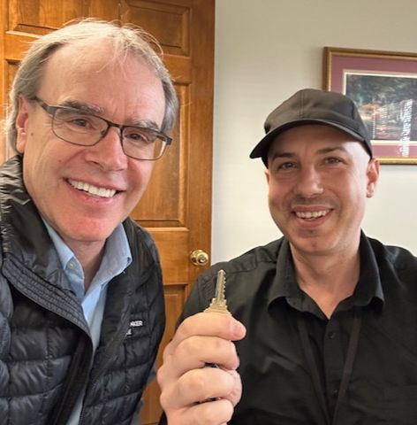 David Campbell, realtor, stands next to Mohammad as they both face the camera, smiling. Mohammad is holding up a house key.