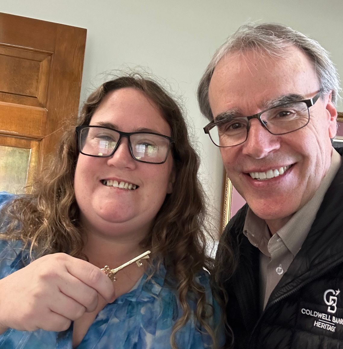David Campbell, local Dayton realtor, stands next to happy client Stacey, as she holds an old-fashioned style house key.