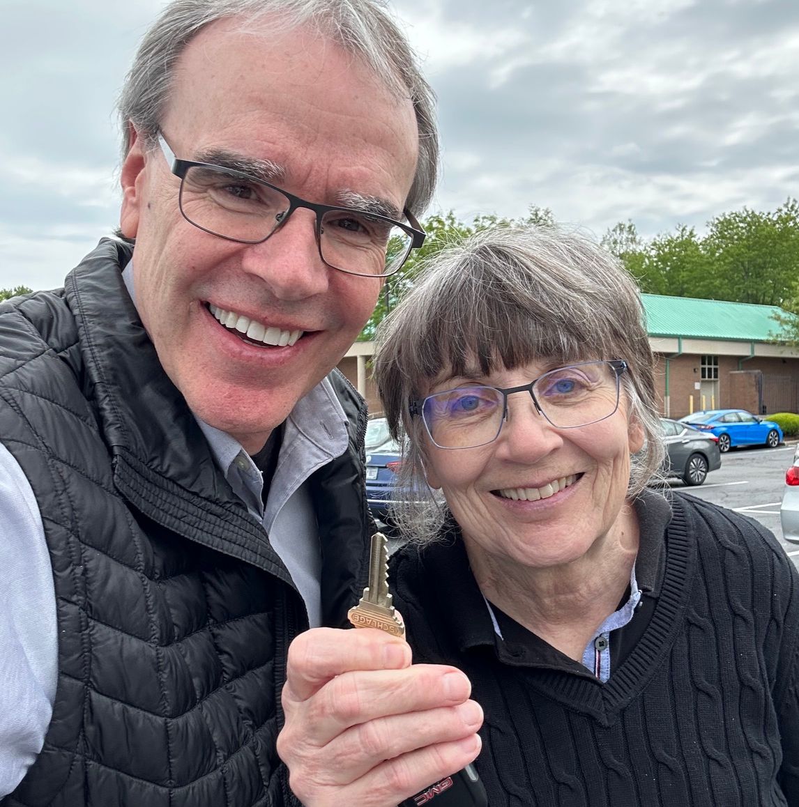 David Campbell, local Dayton realtor, stands next to Cath; they both face towards the viewer, smiling. Cathy is holding a modern house key.