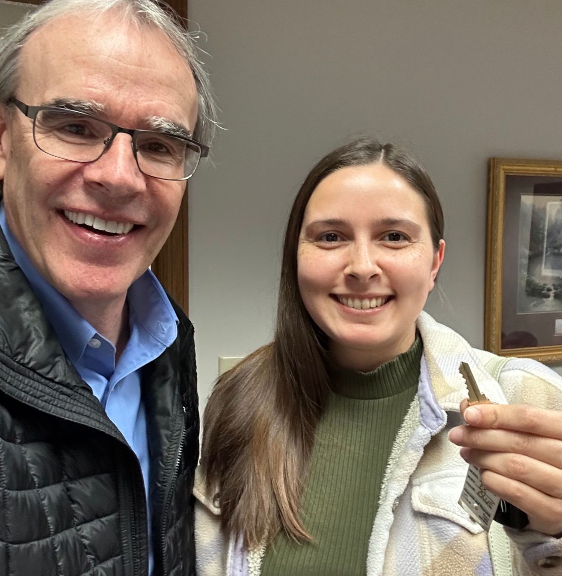 David Campbell, local Dayton, Ohio realtor, stands next to Erica as they both face towards the camera smiling. Erica is holding a house key.